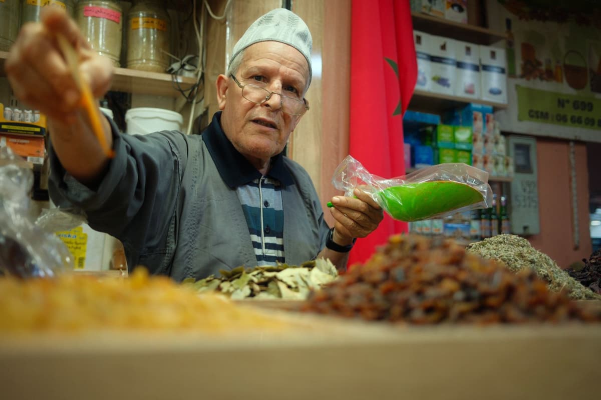 Commerçant marocain servant un client dans son échoppe, drapeau national en arrière-plan
