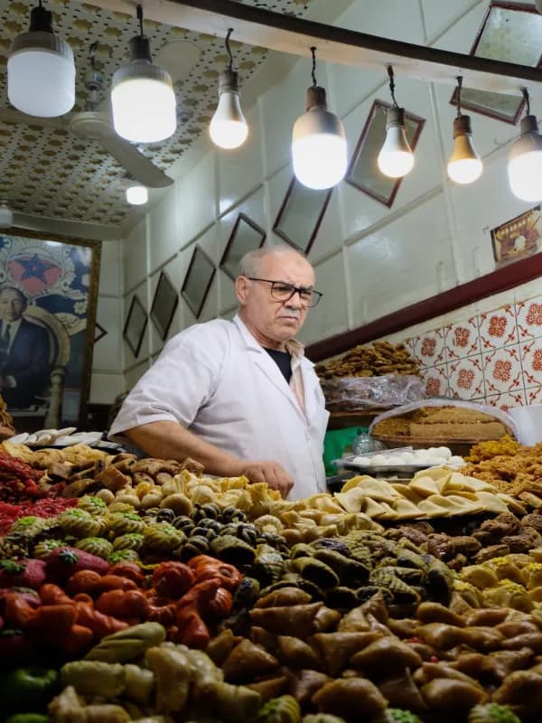 Commerçant marocain dans sa pâtisserie traditionnelle, drapeau national en arrière-plan